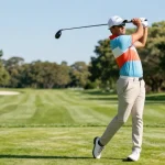 Golfer wearing stylish 골프웨어 레플리카 swinging a driver on a bright golf course with greenery.